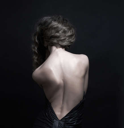 Beautiful woman with long curly hair.elegant lady in black dress. Female back