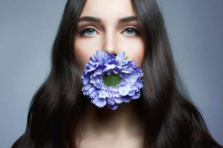 Beautiful Woman with Flower in her Mouth. Beauty Portrait of sensual girl with Blue Flowerの写真素材