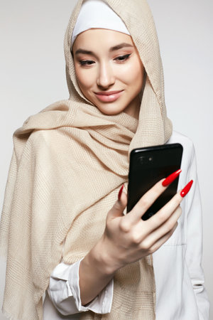 beautiful smiling islamic young woman with smartphone. beauty Happy girl in hijab looking at the screen. fashion oriental style model. asian faceの写真素材