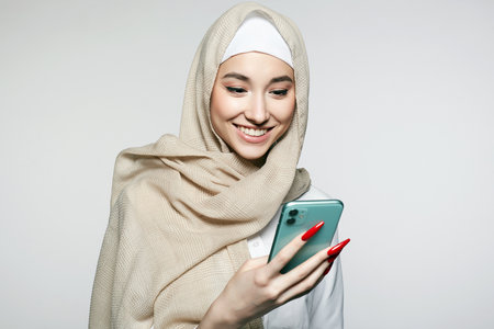 beautiful smiling islamic young woman with smartphone. beauty Happy girl in hijab looking at the screen. fashion oriental style model. asian faceの写真素材