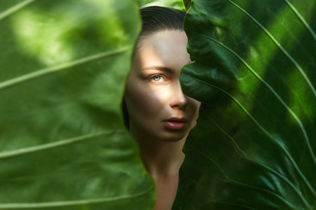 beautiful summer girl behind palm leaves. young woman under palm tree in jungle. Beauty Portraitの写真素材