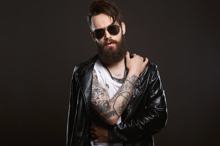 fashionable tattooed handsome man in sunglasses. Bearded man in leather coatの写真素材
