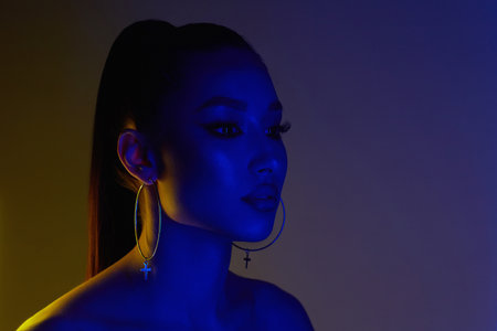 beautiful young woman in color lights. Brunette girl with earrings in neon studioの写真素材