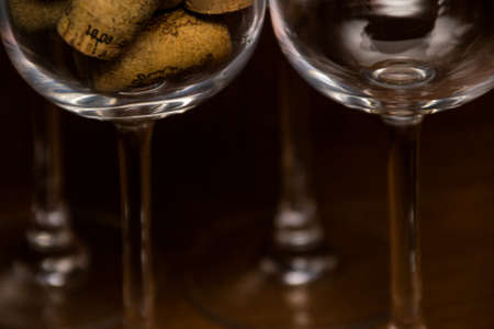 Empty wine glasses and a glass filled with wine corks on a dark woody backgroundの写真素材