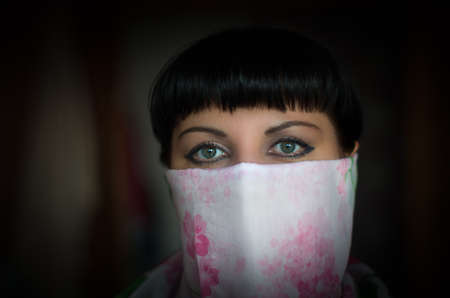 Close-up portrait of a beautiful woman with expressive green eyes, face covered in white and colored scarf. She looks like Scheherazade, the storyteller of One Thousand and One Nights, or a feminist rebel.の写真素材