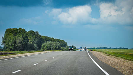 Oncoming traffic with cars, trucks on asphalt road in countryside. Cloudy, stormy sky.の写真素材