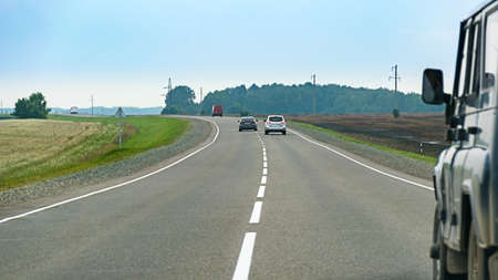 Car chase on asphalt countryside road winding through the fields and green trees on a summer...