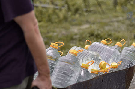 Water supply shortage and climate change threats. White male pulls a cart of plastic bottles filled with clean water from a public pump to his familys house.の写真素材