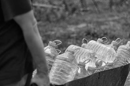 male pulls a cart of plastic bottles filled with clean water from a public pump to his familys house.の写真素材