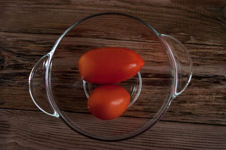 Top view of red tomatoes in a glass bowl on rustic dark wooden tableの写真素材