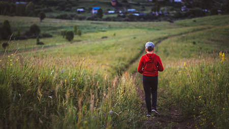Teenage boy in red jacket walking home along downhill country road on sunset