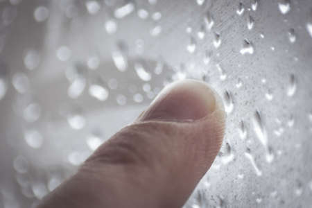 Moody Feelings Concept: Finger Of A Teenager Drawing On The Window With Raindrops On A Rainy Dayの写真素材