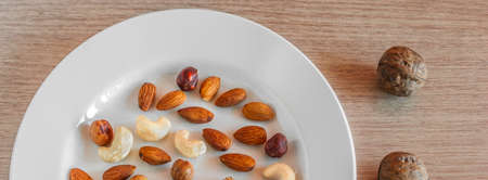 Mix of Almonds, Hazelnuts, Walnuts, Cashew Nuts on a White Plate, and Three Whole Walnuts on Light...