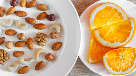 Assorted Nuts, Orange Slices On White Plates On Wooden Table. Healthy Organic Snack, Breakfast, Food Ingredients. Flat Lay Top-Down Composition.の写真素材