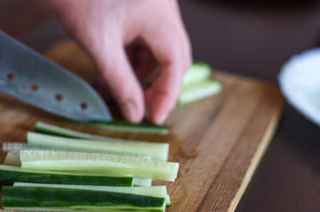Woman's Hands Cut Cucumber Matchsticks with Santoku Knife on a Wooden Chopping Board.  Salads, Maki and Temaki Sushi Rolls Ingredientの写真素材