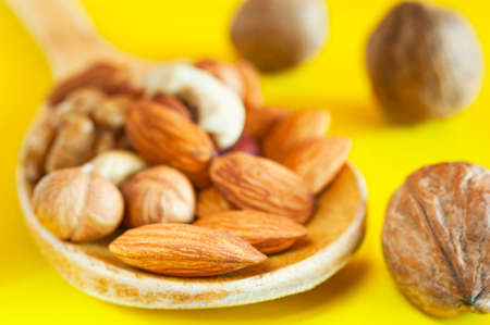 Almonds, Hazelnuts, Walnuts, Cashew Nuts in a Wooden Spoon, and Three Whole Walnuts Isolated on Yellow Background. Healthy Organic Snack, Breakfast, Food Ingredients.の写真素材