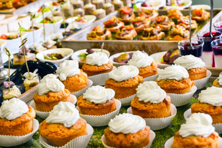Catering Services Concept: Vanilla Cupcakes Topped With White Cream, Various Snacks Served at a...