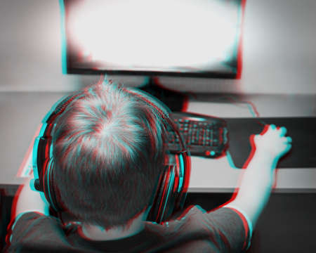 Back of the head view of a teenager playing a computer game at home. He is wearing a headset. The...