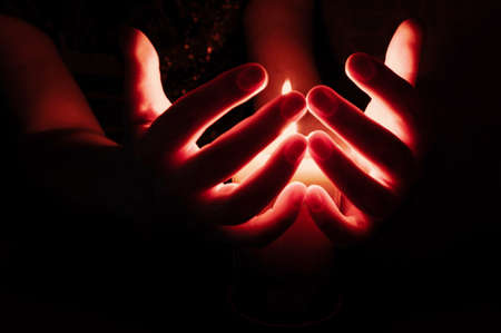 Female Hands, Fingers Splayed Out, Around Burning Candle at Night.の写真素材