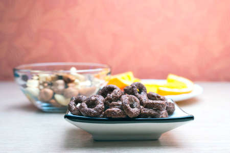 Crunchy Chocolate Cereals Round Oats in a Dish, Glass Bowl of Nuts and Orange Slices in a White...