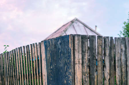 Old Rustic Wooden Board Fence with the Roof of a House and Garden behind At Sunsetの写真素材
