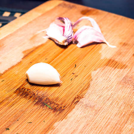 Single Peeled Garlic Clove, Skin on a Wooden Cutting Board. Organic Food Concept.