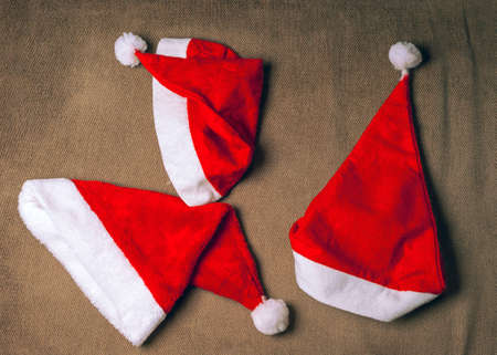 Three Santa Hats on Wrinkled Brown Fabric Backgroundの写真素材