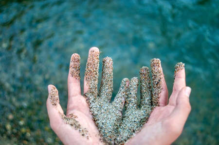 Two Hands Together Partially Covered with Wet Coarse Sand, Water Waves in Background.の写真素材