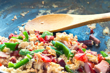 Scrambled Eggs with Tomatoes, Green Peppers, Ham and Salami in a Frying Pan with Wooden Spoon. Easy Cooking Concept.の写真素材