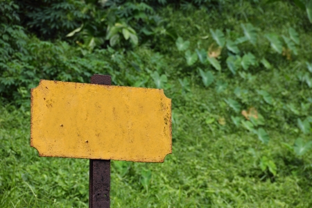 Closeup of an old blank yellow railway sign showing signs of rusting. With vegetation as background.の写真素材