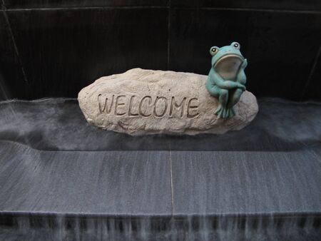 A waterfall feature with a stone "Welcome" sign and a frogの写真素材