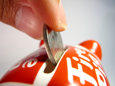 A hand inserting a coin into a piggy bank. On whiteの写真素材
