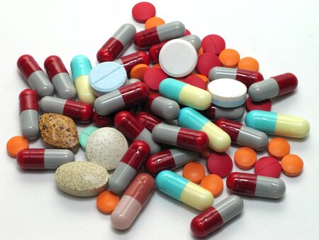 A pile of tablets and pills piled closely together  On a white background with shadows 