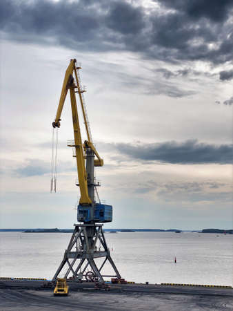 Yellow arrow of a harbor crane. Photo in the sky, equipment in the seaport. City landscape,...
