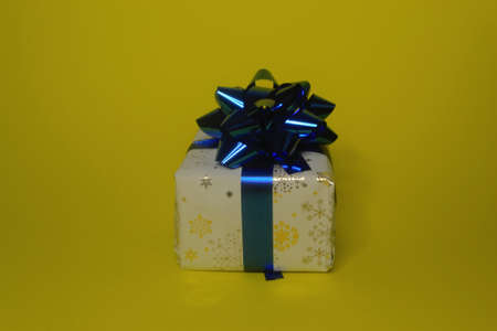 Gift colorful box with blue ribbon bow close-up on a bright yellow background.