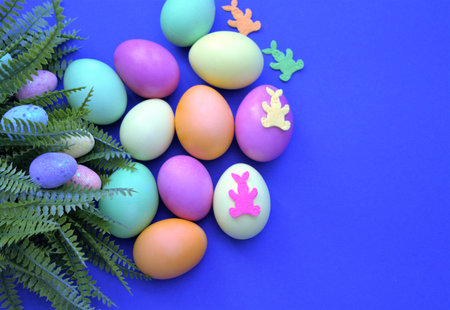 Colorful Easter eggs. Banner, wallpaper, postcard, social media post with copy space for text. Painted eggs, located on one side on a dark purple background, green leaves of the plant.の写真素材