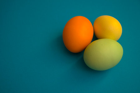Three colored eggs lie on a purple background. Easter minimal composition. Holiday card with eggs. copy space, flat layの写真素材