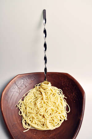boiled spaghetti in a large brown clay dish with a large forkの写真素材