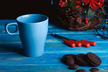 A blue cup with chocolate and biscuits with a Christmas decor on the table