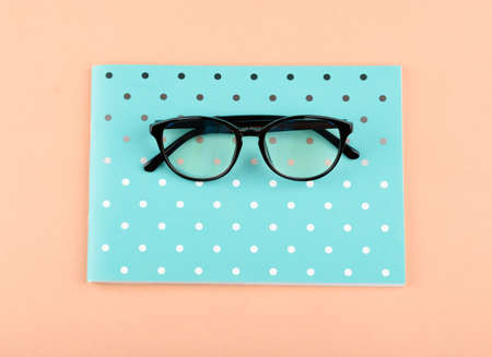A beautiful notepad with black glasses on a colored background.