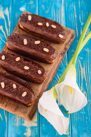 Delicious chocolate and peanut eclairs on a blue wooden table with white calla flowers