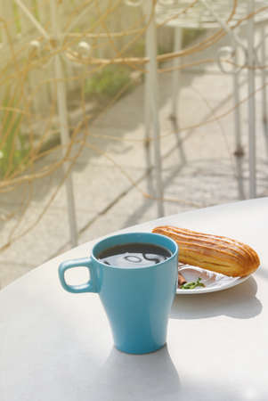 Aromatic coffee in a blue cup with eclairs in a summer cafe. Spring, cinnamon, leaf sprigs.