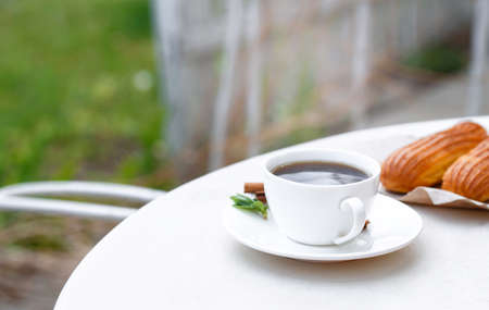 Fragrant coffee in a white cup with eclairs in a summer cafe. Spring, cinnamon, leaf sprigs.