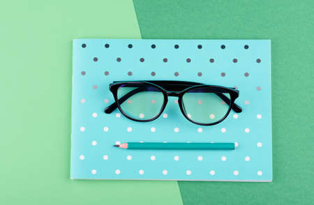 Beautiful blue notebook with a pencil, glasses, on a green backgroundの写真素材