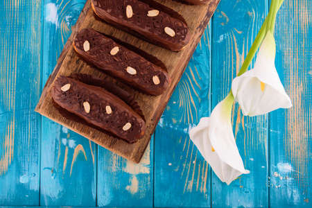 Delicious chocolate and peanut eclairs on a blue wooden table with white calla flowers
