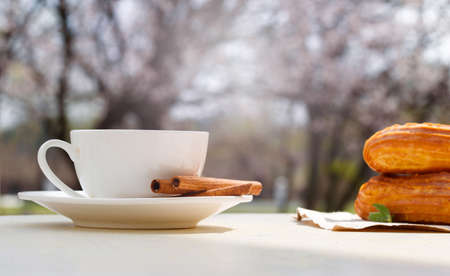 Fragrant coffee in a white cup with eclairs in a summer cafe. Spring, cinnamon, leaf sprigs.の写真素材