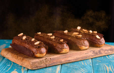 Tasty eclairs with chocolate and peanuts on a blue wooden table. Sparkles