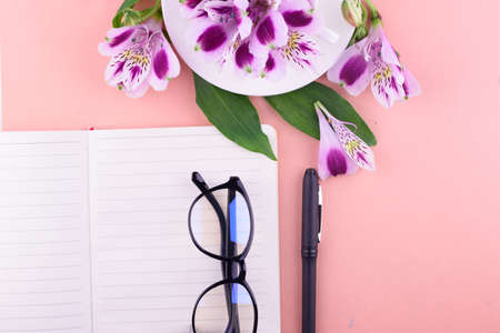 View from above. Fragrant tea in a white cup, beautiful flowers, a pink background, a notebook with...