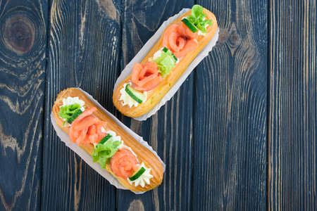 Tasty and beautiful eclairs on a wooden board. Appetizing dessert with red fish, cucumber, cheese...
