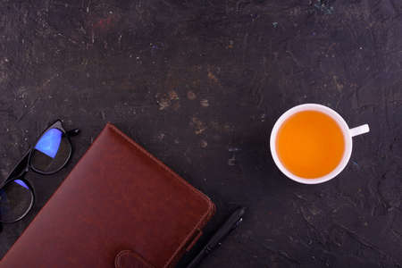 View from above. Fragrant tea in a white cup, beautiful flowers, a black background, a notebook with...
